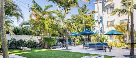 A courtyard with palm trees, outdoor seating, and string lights.