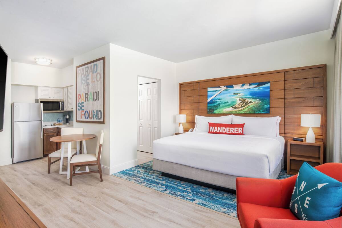 A hotel room with a bed, a desk, a chair, a microwave, and a refrigerator.
