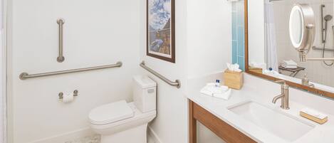 A bathroom with a toilet, bidet, handrails, a sink with a mirror, and a framed picture on the wall.