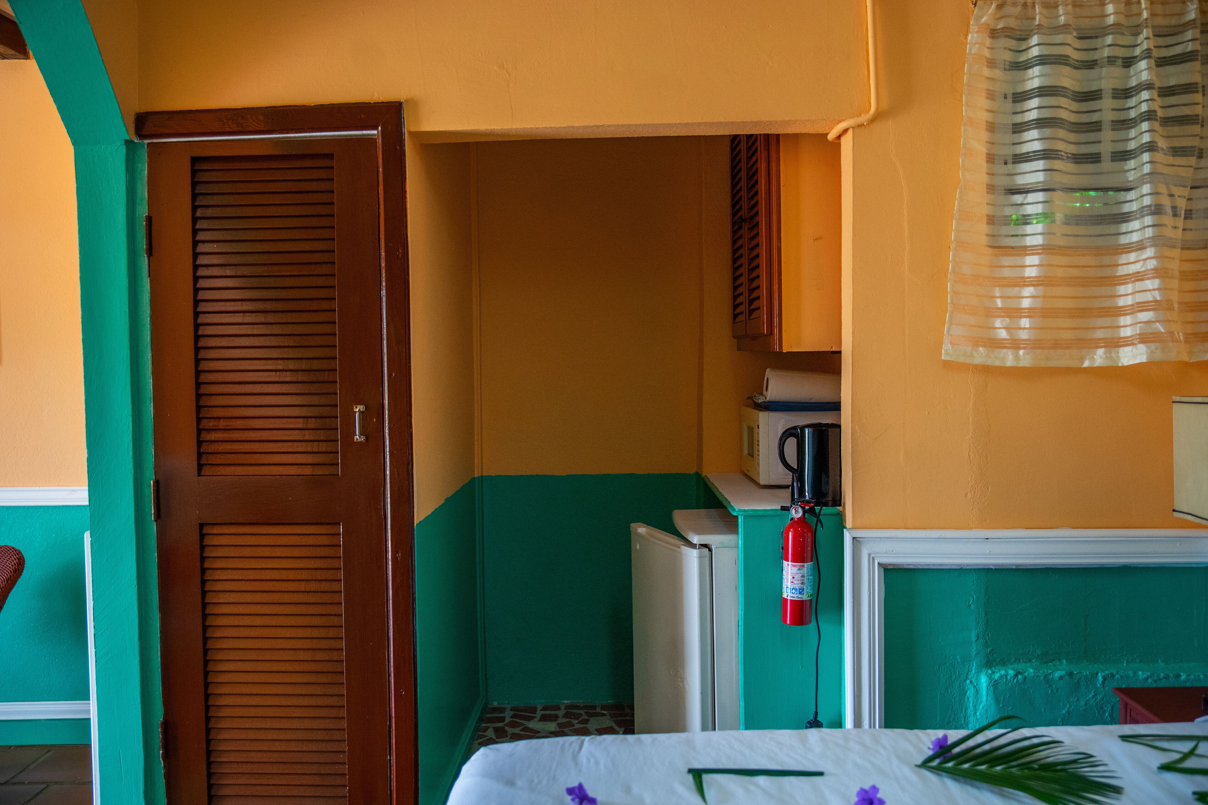 A compact room with a bed, a small kitchenette, a door, and a fire extinguisher.