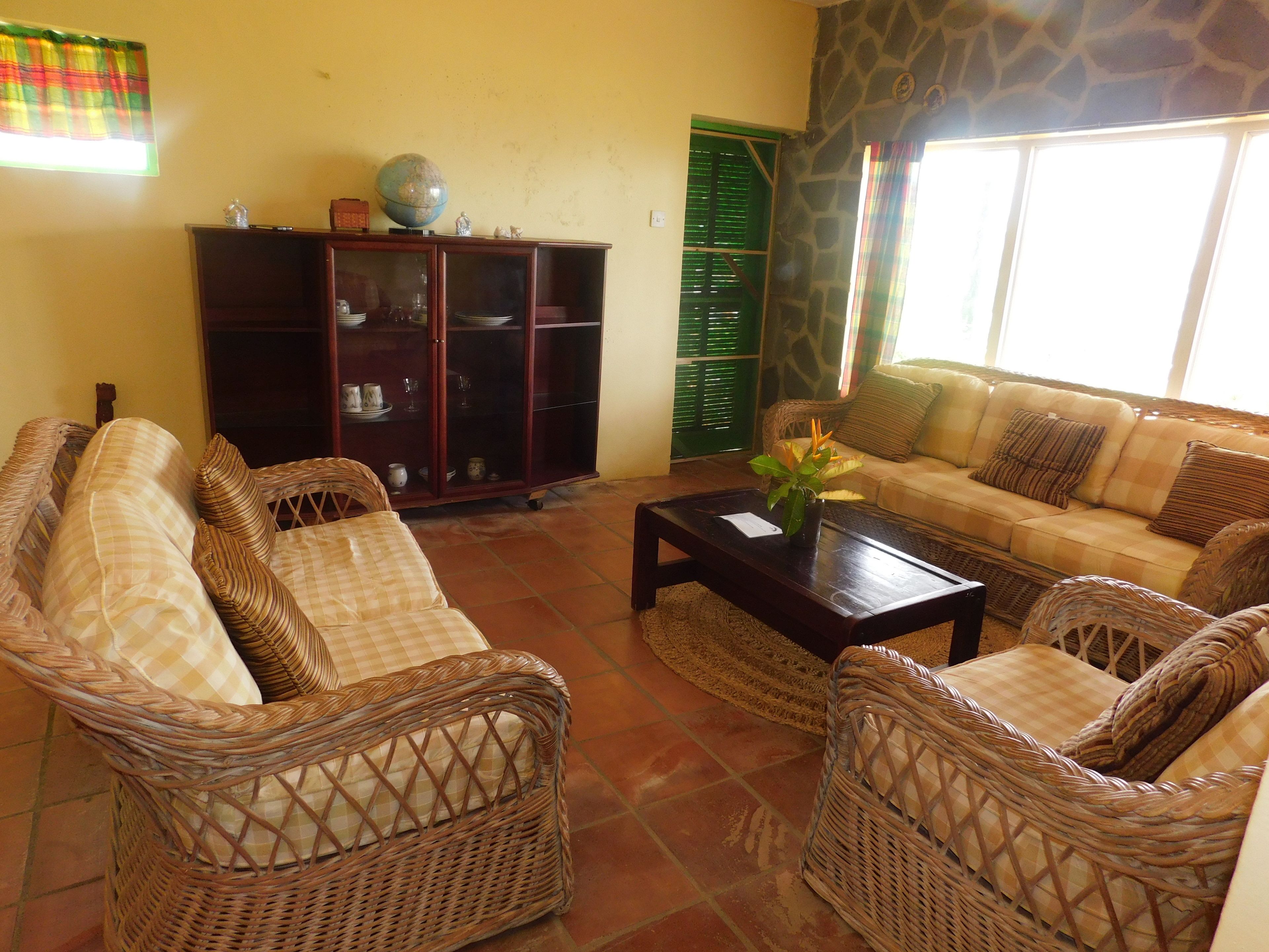 A living room with wicker furniture, a globe on a cabinet, and a window with shutters.