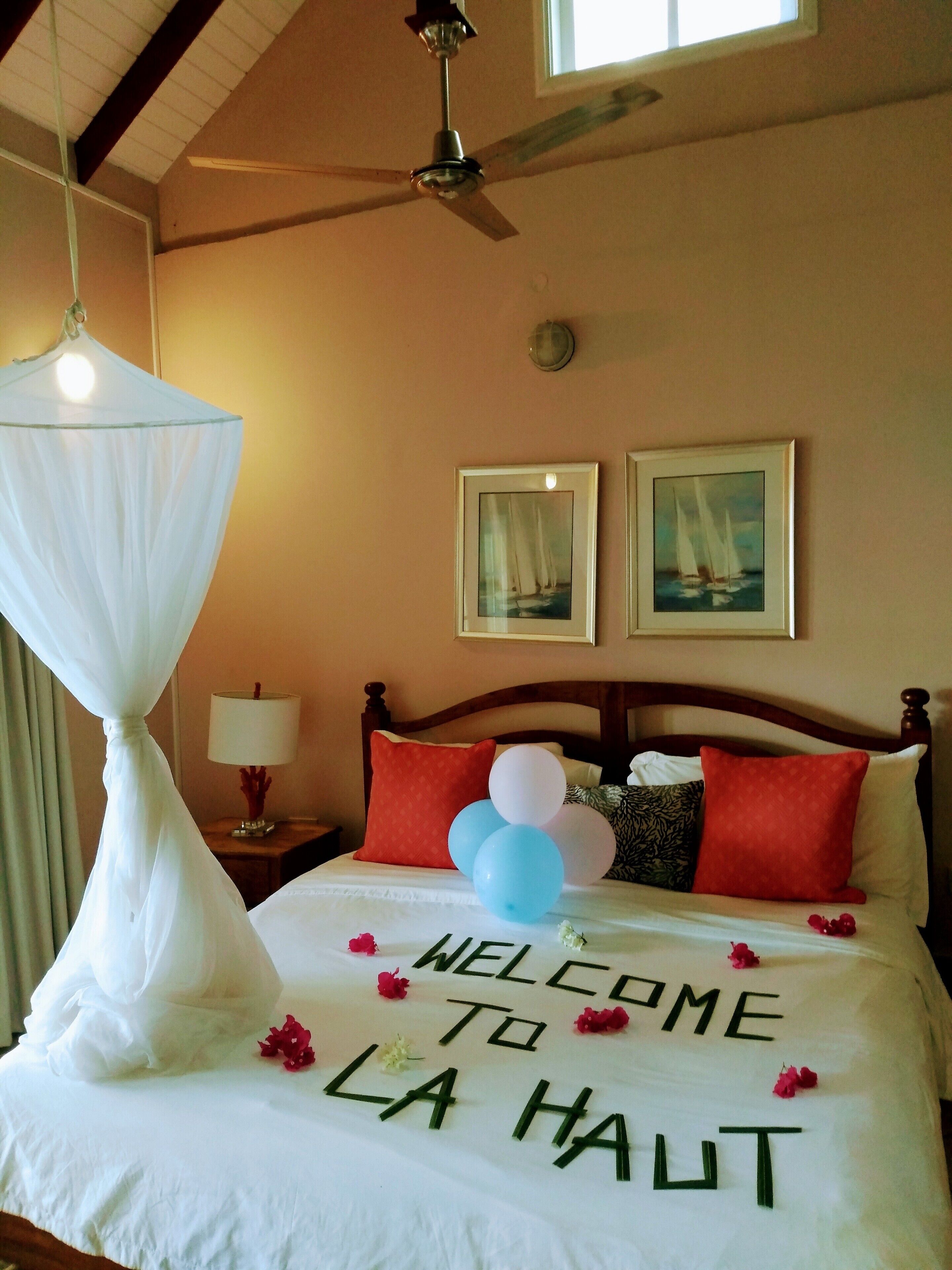 A hotel room with a bed, a ceiling fan, a nightstand with a lamp, and two framed pictures on the wall.