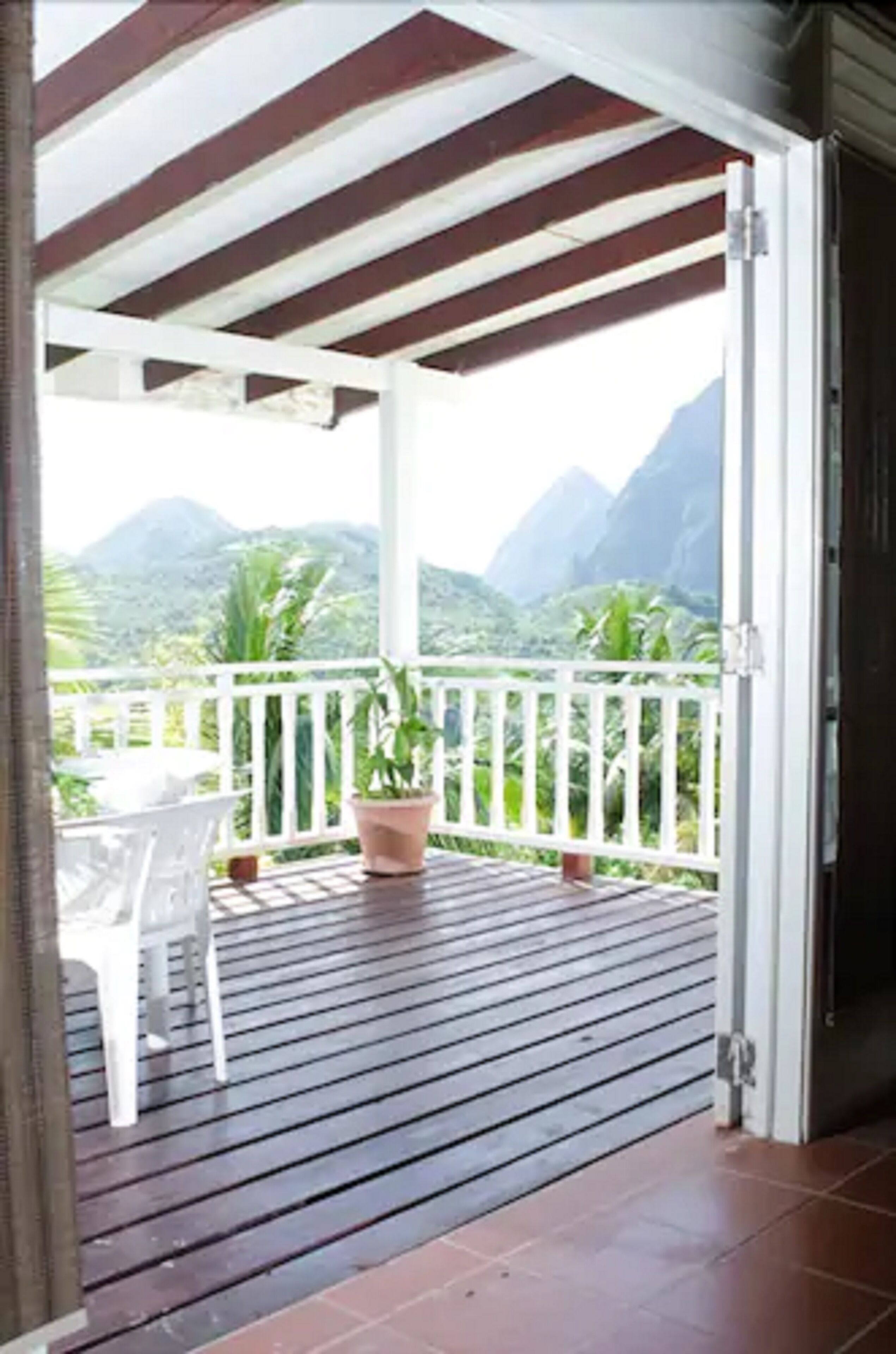 Un espace extérieur abrité doté d’une terrasse en bois, d’une rambarde blanche et d’une plante en pot.