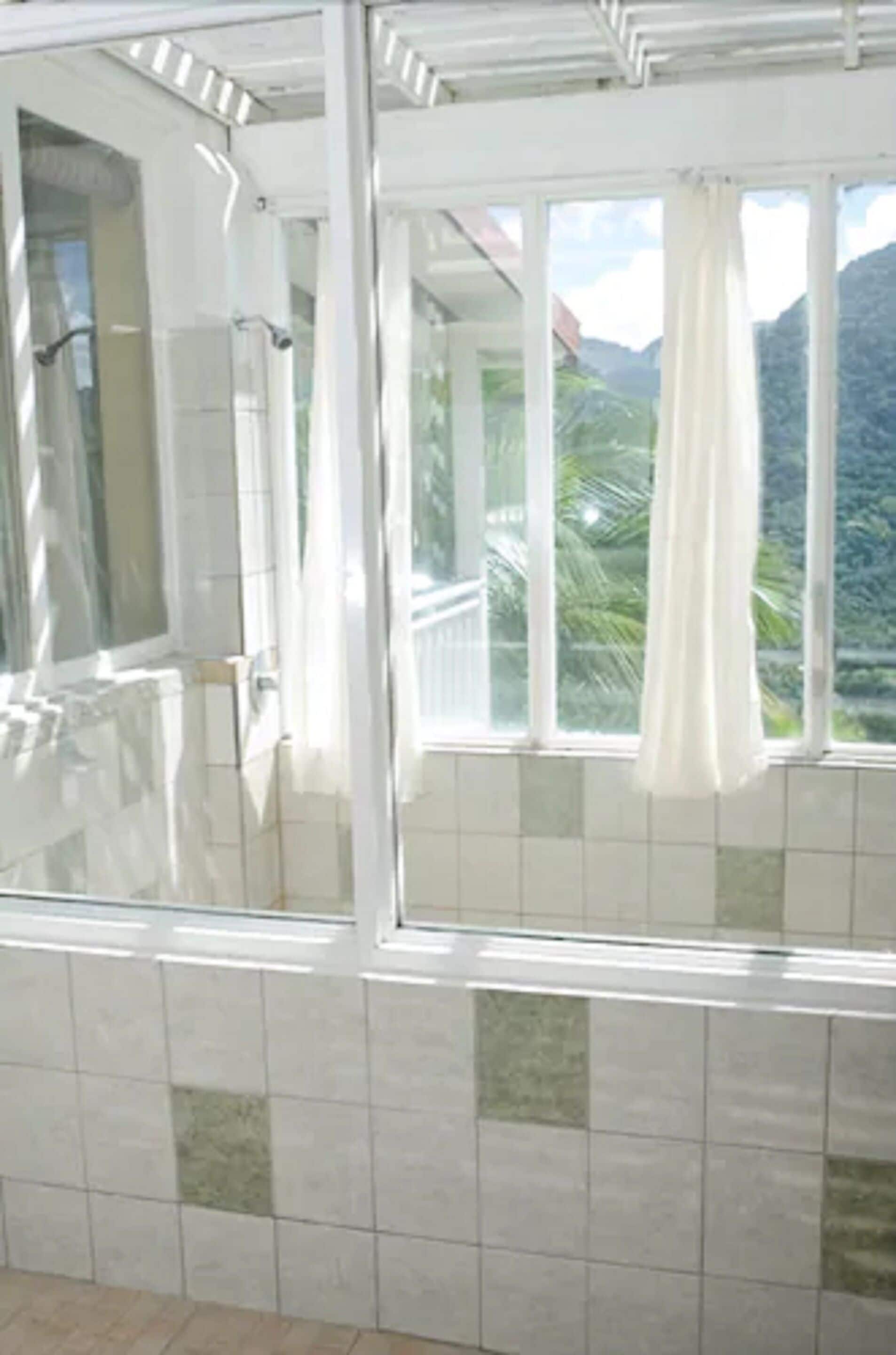A bathroom with a glass shower enclosure, a tiled floor, and a view of mountains through large windows.