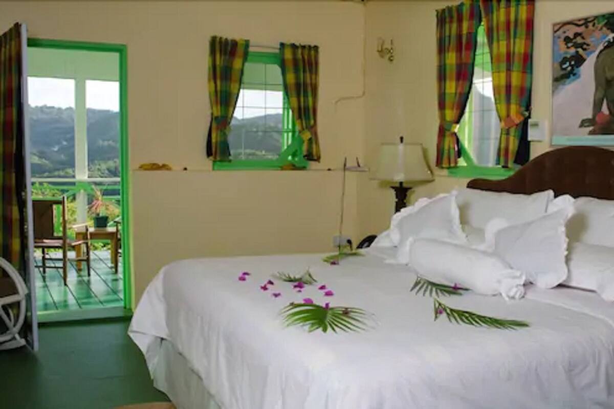 Una habitación de hotel con cama, una silla, ventana con cortinas y vistas al exterior.