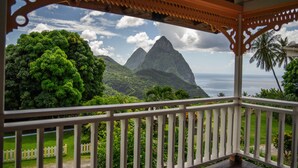 Vista desde un balcón cubierto con barandilla blanca, que da a un paisaje exuberante con una montaña destacada y palmeras.