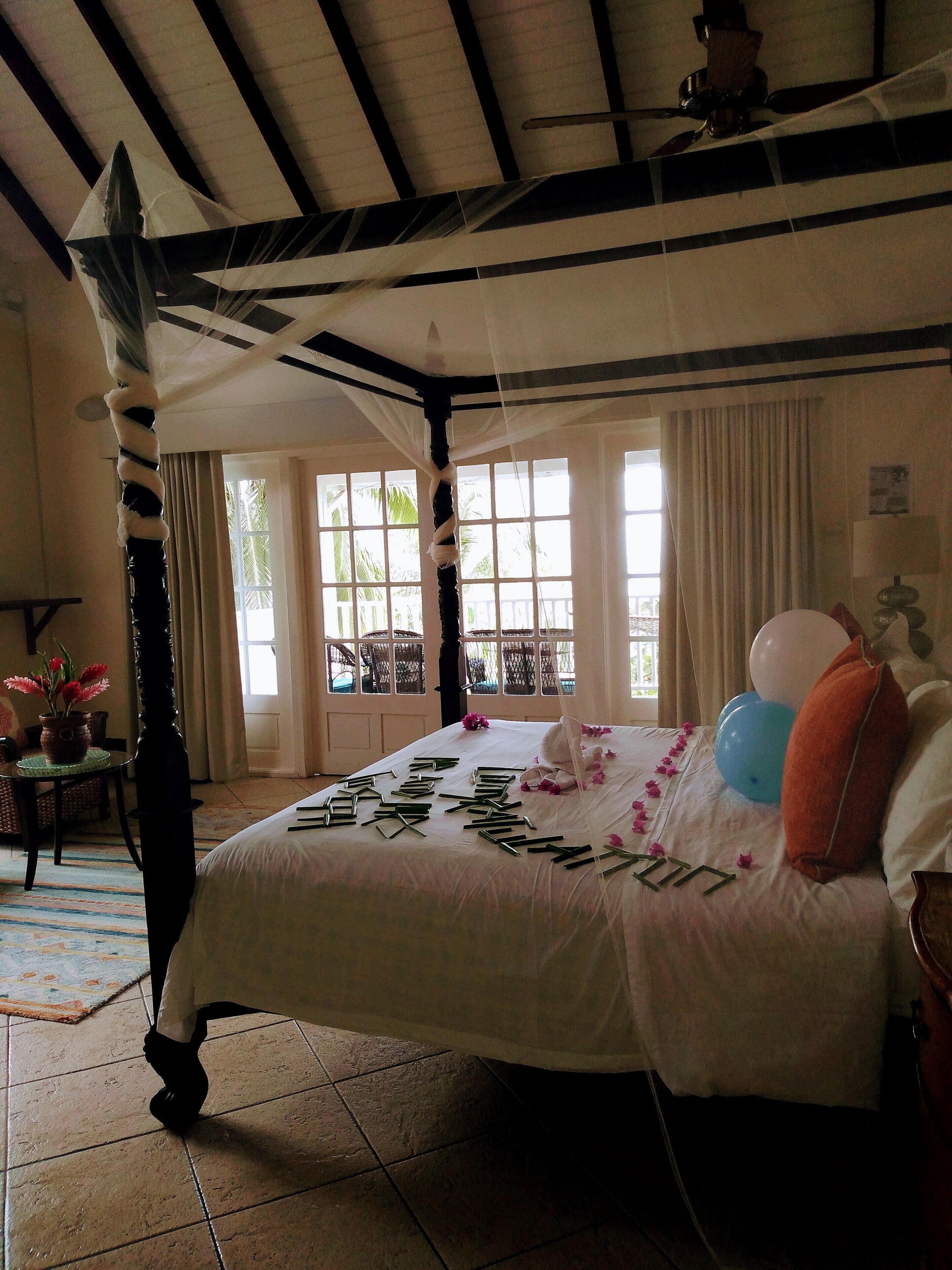 Un dormitorio con cama con dosel, una ventana con cortinas y vista a palmeras.
