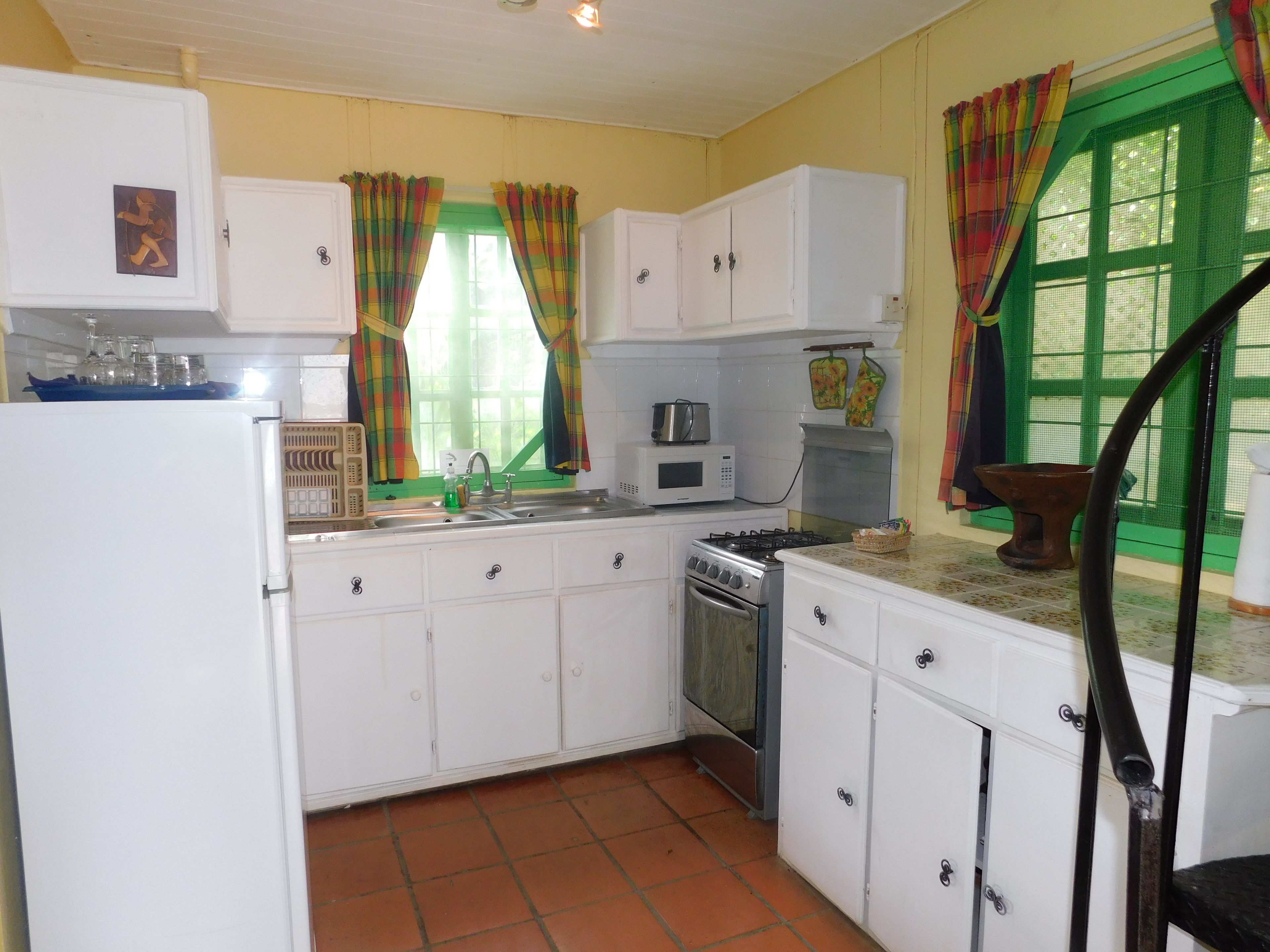 A kitchen with white cabinets, a stove, a sink, and a window with colorful curtains.