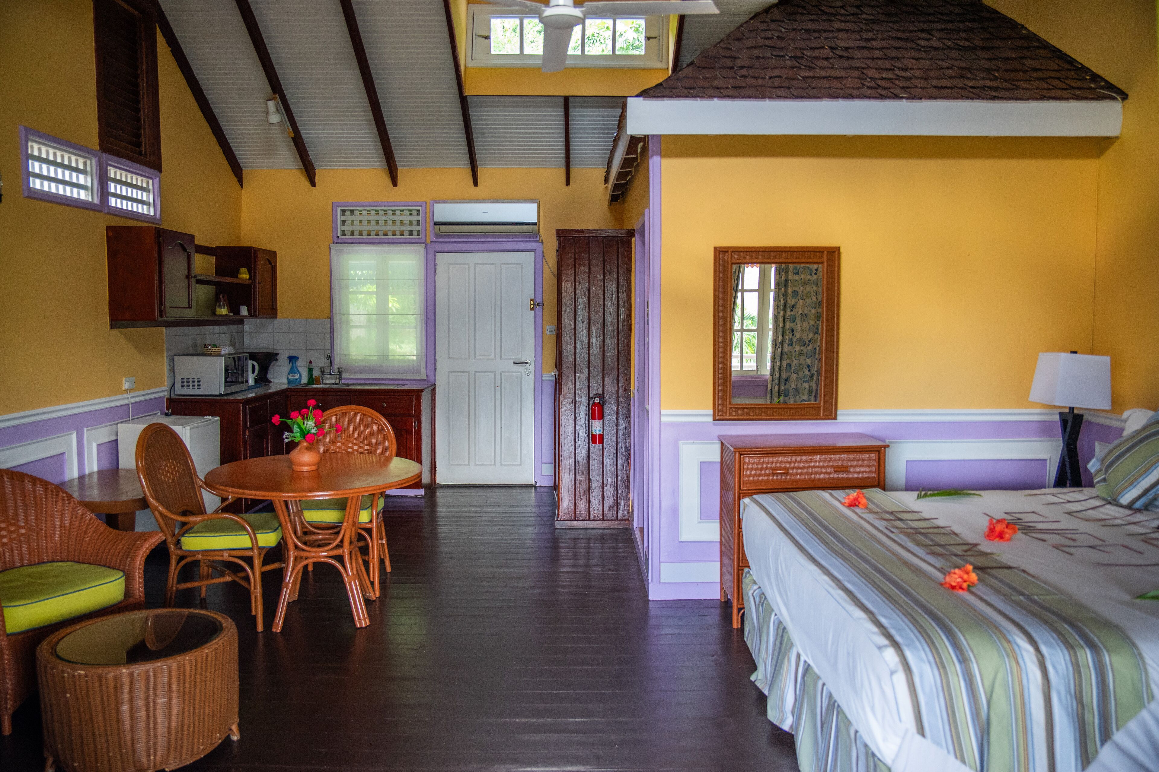 A room with a bed, a dining table with chairs, a small kitchen area, and a door leading to another room.