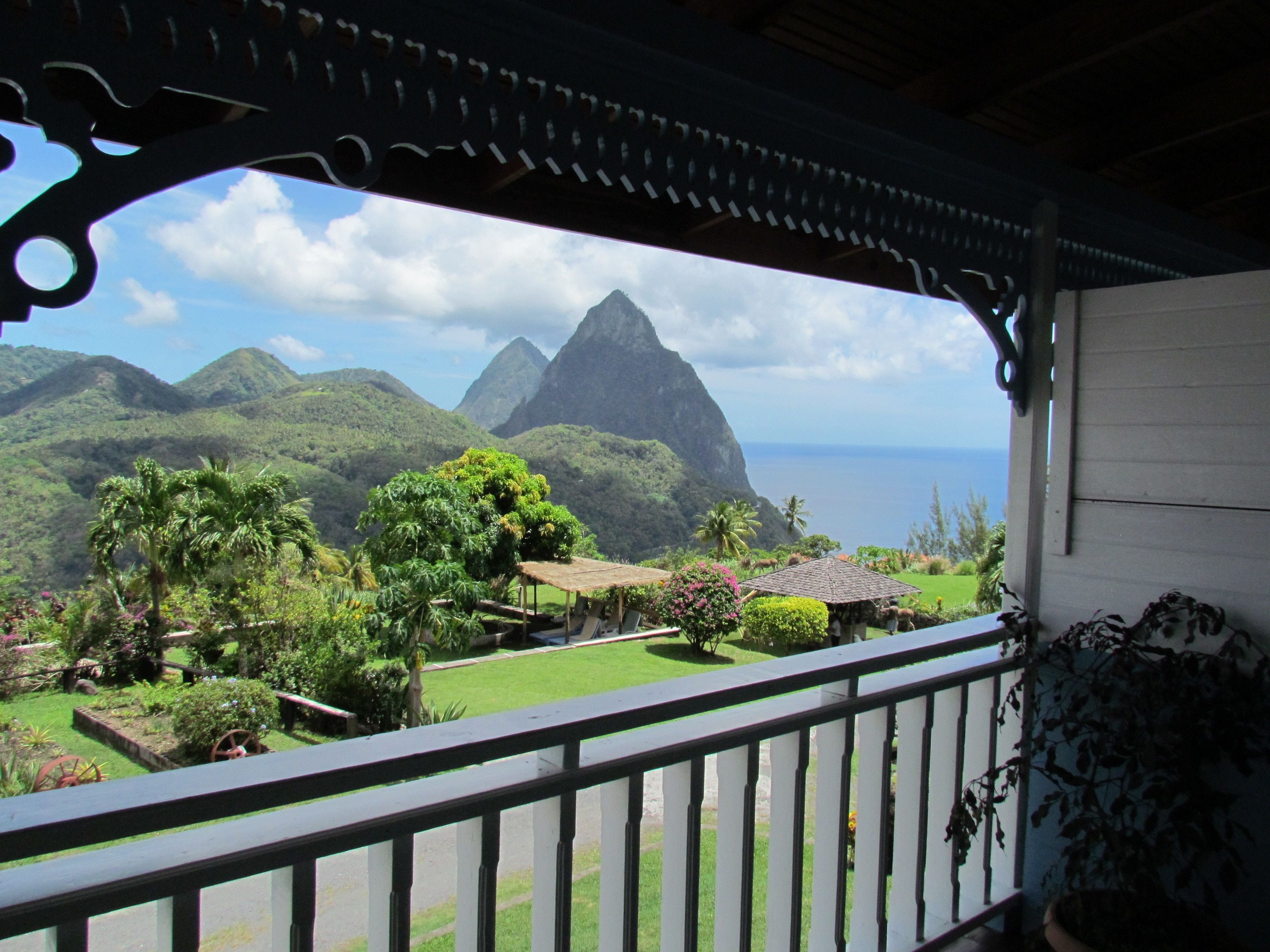 A balcony with a view of lush greenery, a mountain, and the ocean.