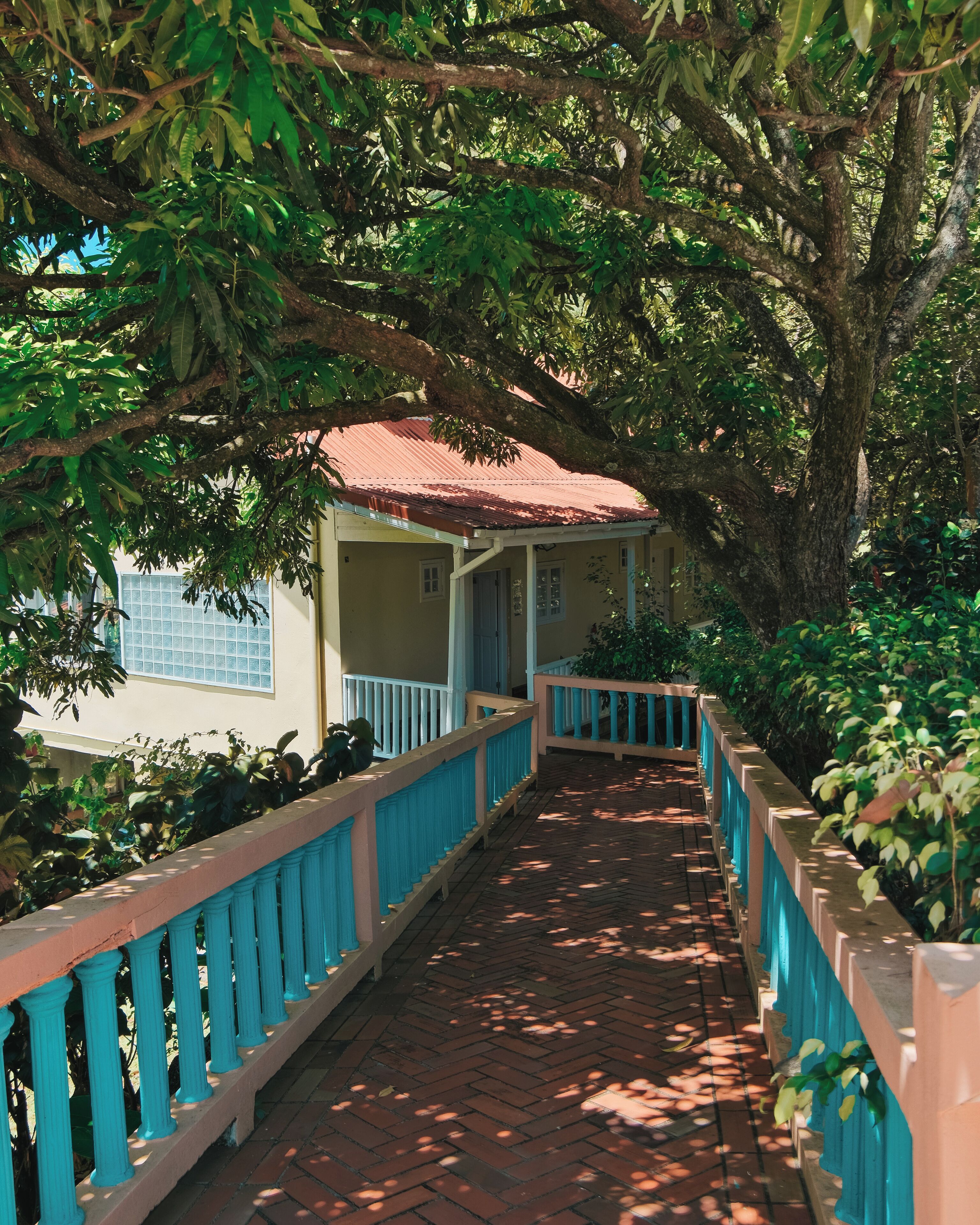 A covered walkway with a red roof, bordered by blue railings, leading to a building with a light yellow facade and a red roof.