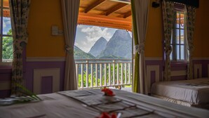 Una habitación con cama, ventana con cortinas y vista a montañas.