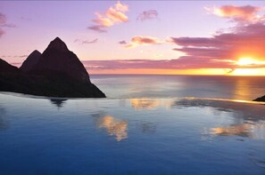 A coastal landscape with a sunset, calm sea, and mountain silhouettes. - La Haut Resort (Soufrière)
