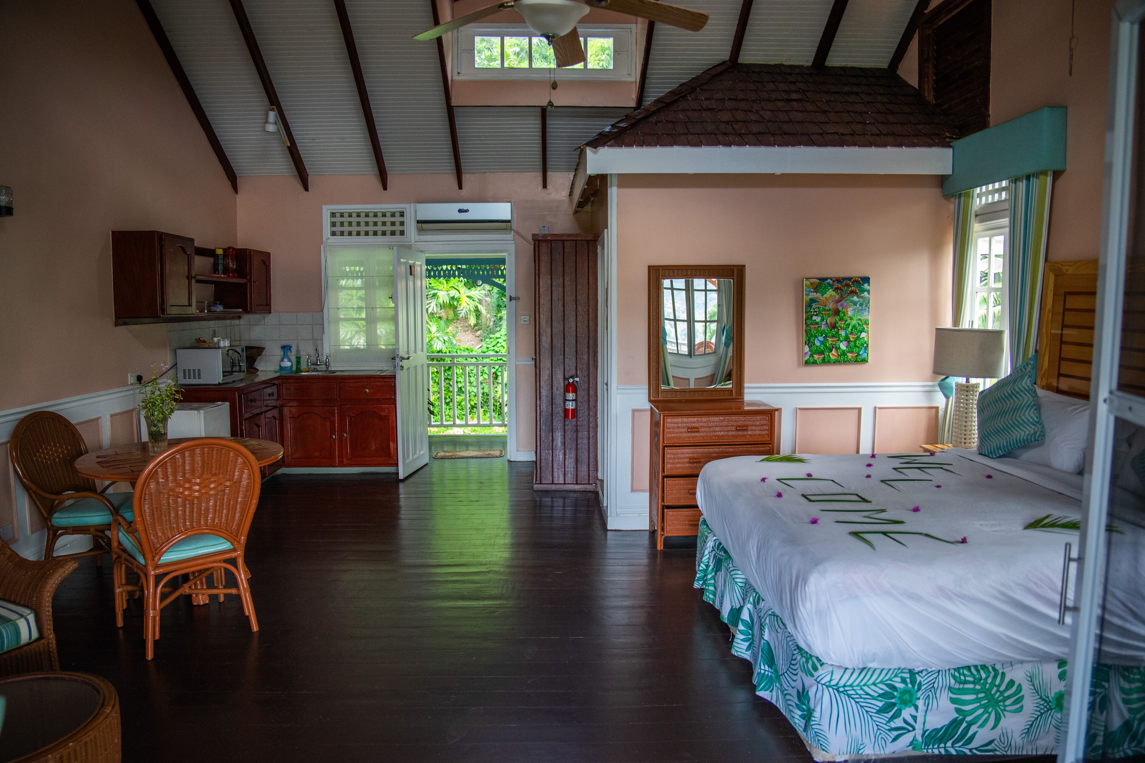 A room with a bed, a dining table with chairs, a kitchen area, and a balcony.