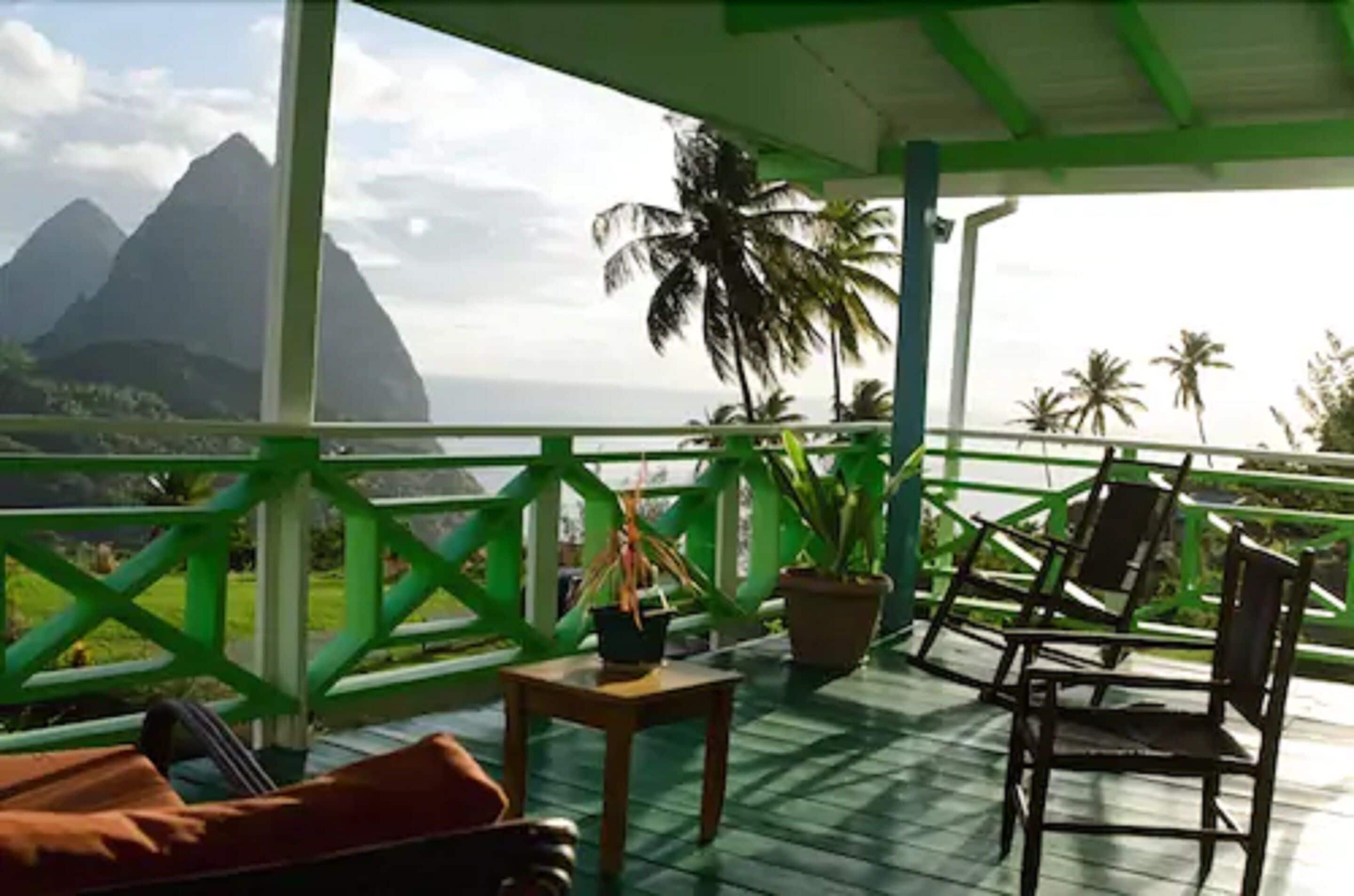 A balcony with a view of mountains and palm trees, wooden furniture, and potted plants.