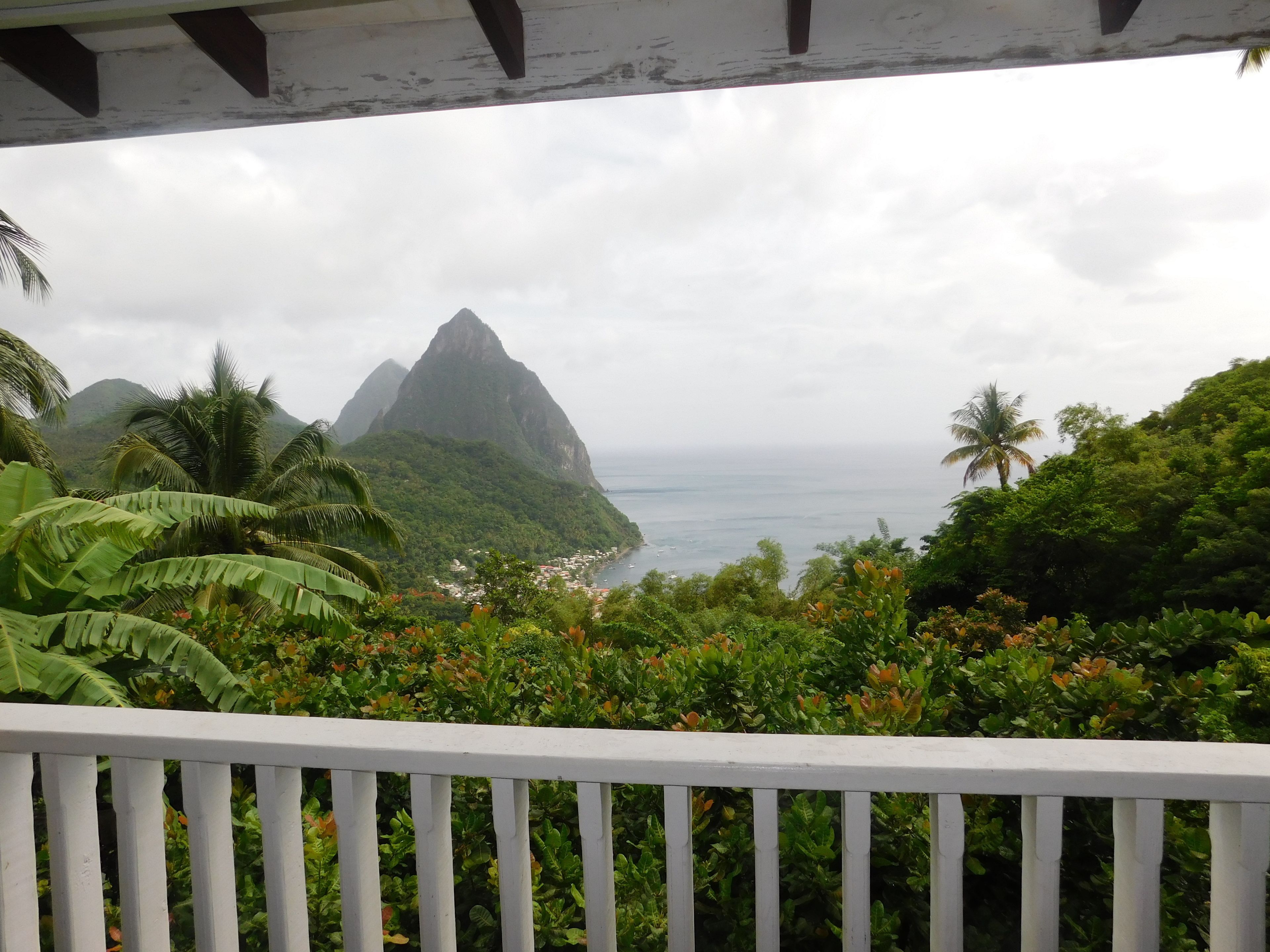 A view from a balcony with a railing, overlooking a coastal area with mountains and dense greenery.