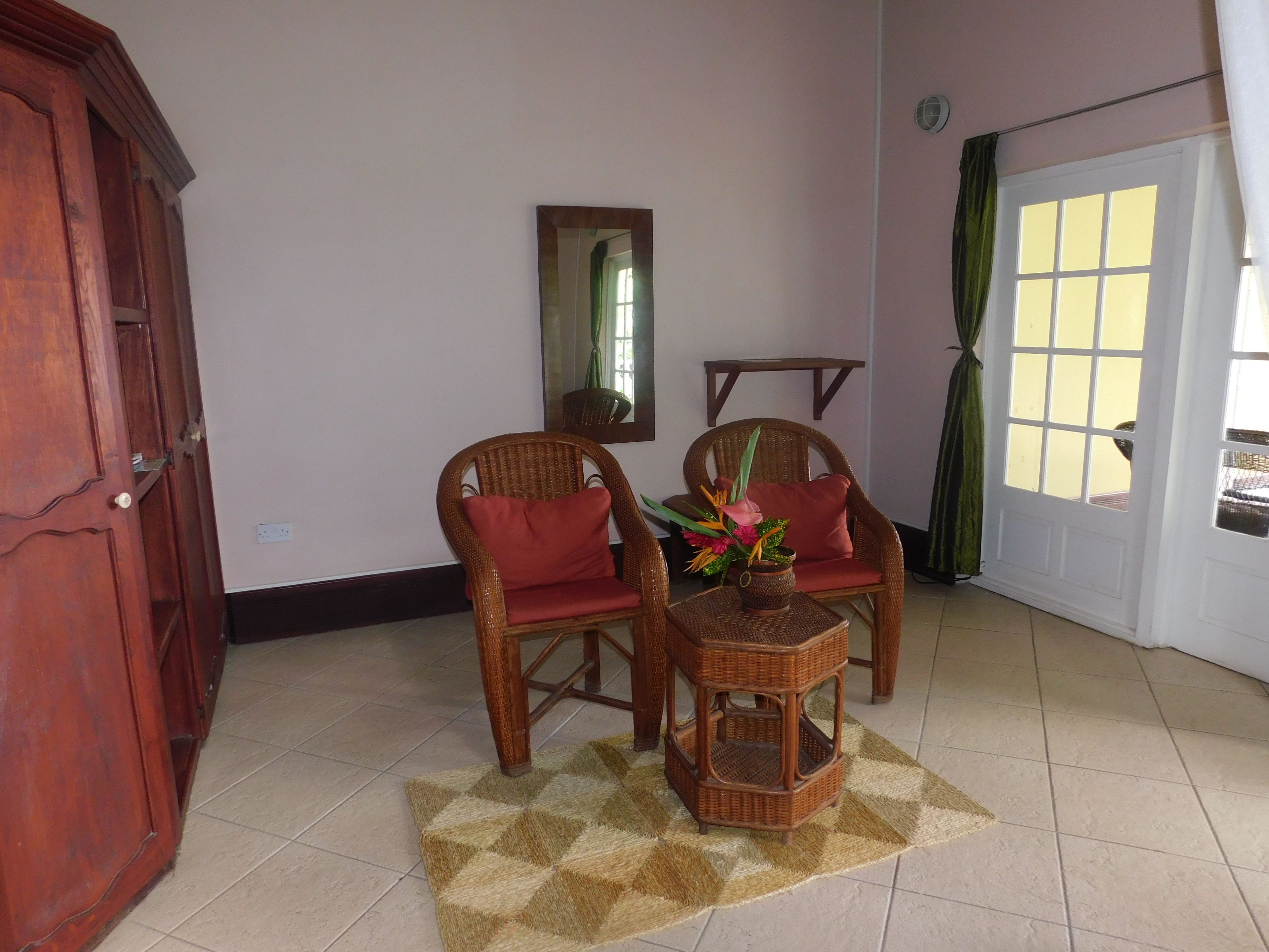 Una habitación con dos sillas de mimbre, una mesita, un espejo y una puerta con cortina verde.