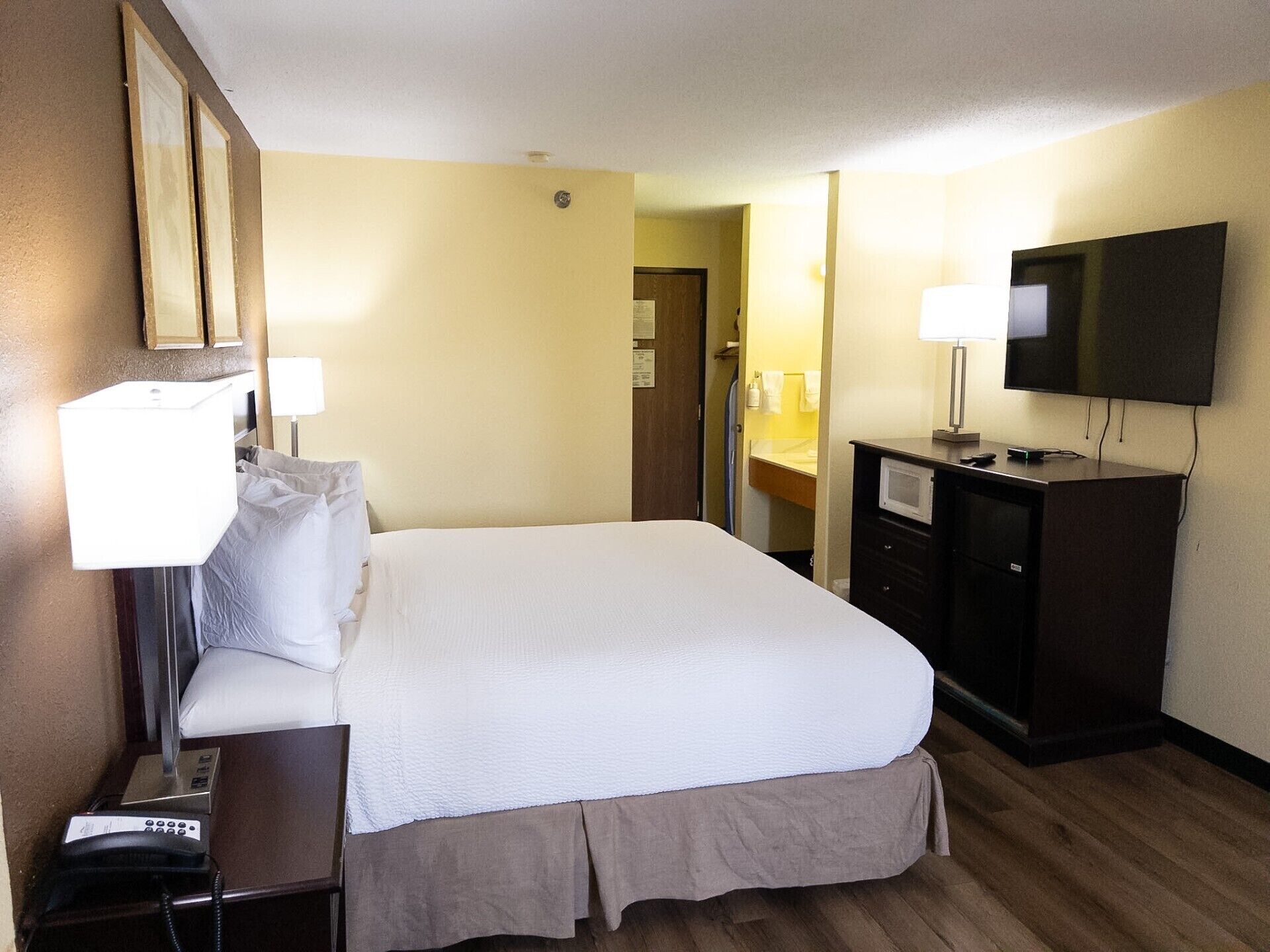 A hotel room with a bed, bedside lamps, a television, a desk with a telephone, and a mirror.