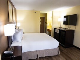 A hotel room with a bed, bedside lamps, a television, a desk with a telephone, and a mirror.