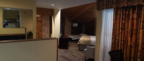 Une chambre d’hôtel avec un plafond en bois, un lit, un bureau, une chaise, un miroir et un téléviseur.