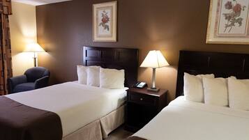 A hotel room with two beds, a chair, a nightstand with a lamp, and two framed floral pictures on the wall.