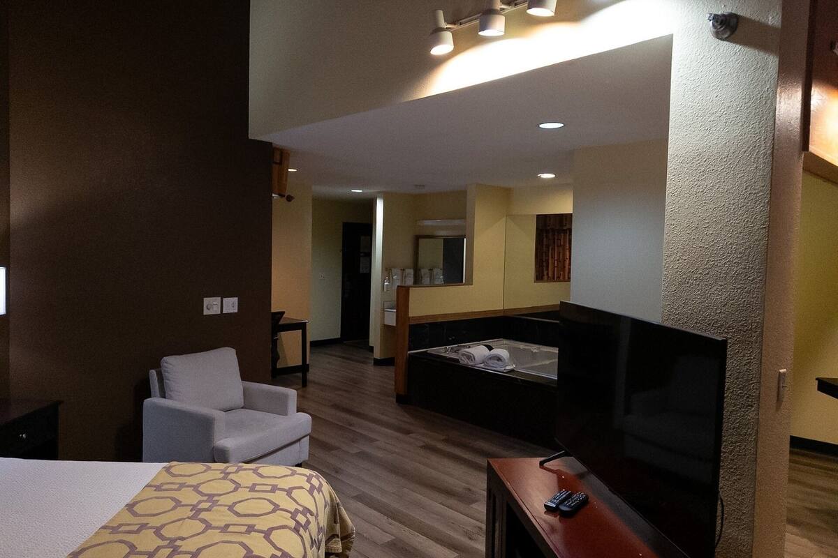 A hotel room with a bed, a desk, a chair, a TV, and a bathtub.