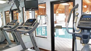 Ein Fitnessstudio mit Laufbändern und einem Pool, der durch die Tür sichtbar ist.