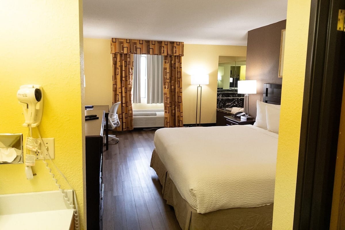 Ein Hotelzimmer mit Bett, Schreibtisch, Stuhl, Lampe, Spiegel und Haartrockner.