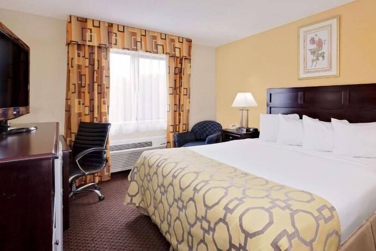 Ein Hotelzimmer mit Bett, Schreibtisch, Stuhl, Fernseher, Lampe und einem Fenster mit Vorhängen.