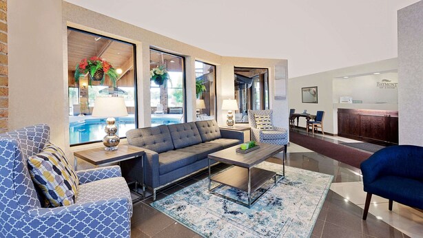 Eine moderne Hotellobby mit grauem Sofa, gemusterten Sesseln, einem Couchtisch und einer Rezeption.