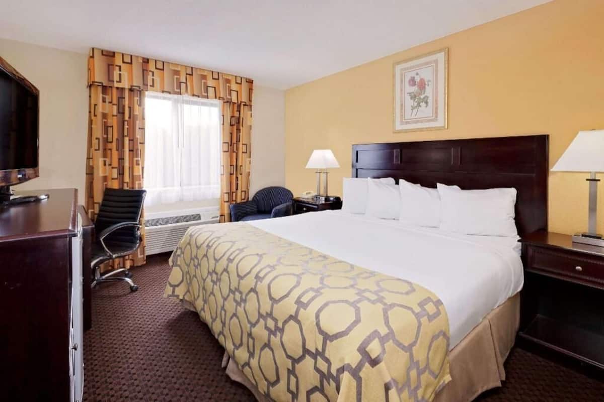 Ein Hotelzimmer mit einem großen Bett, einem Schreibtisch, einem Stuhl, einem Fernseher und einem Fenster mit Vorhängen.