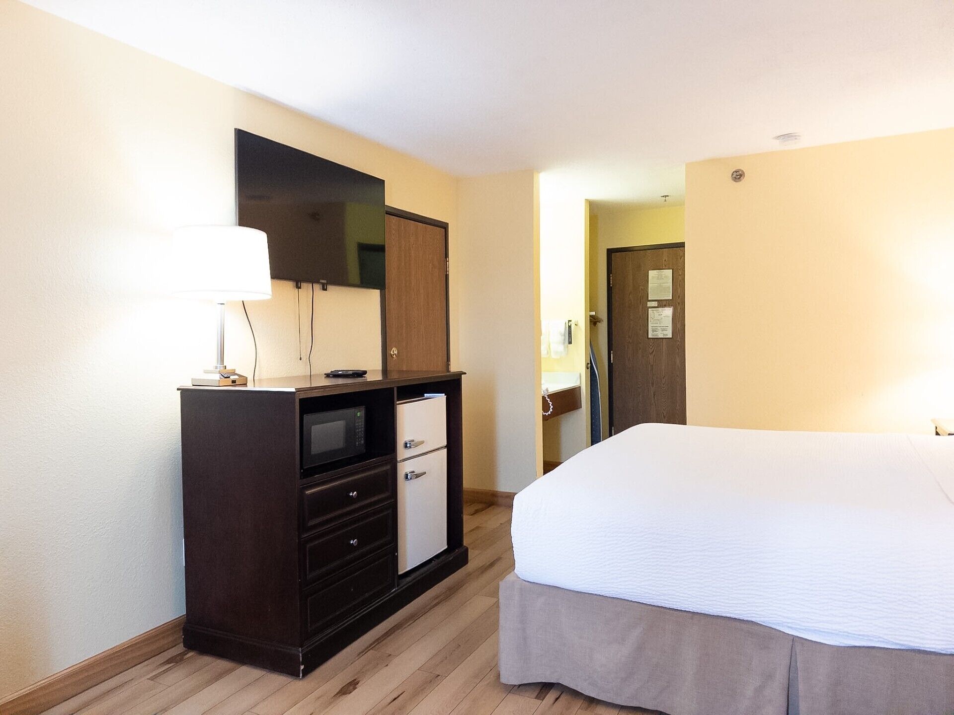 Een hotelkamer met een bed, een dressoir met een magnetron, een lamp en een deur naar een badkamer.