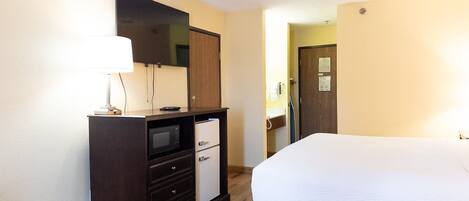 Een hotelkamer met een bed, een dressoir met een magnetron, een lamp en een deur naar een badkamer.