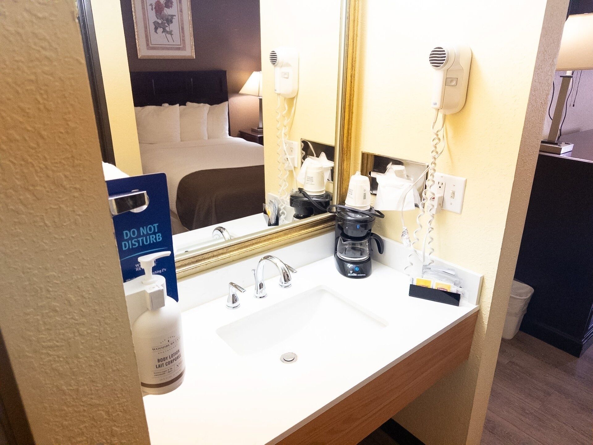 A hotel bathroom with a white sink, a mirror, a hairdryer, and a coffee maker.