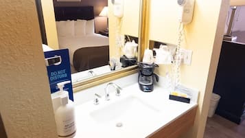 A hotel bathroom with a white sink, a mirror, a hairdryer, and a coffee maker.