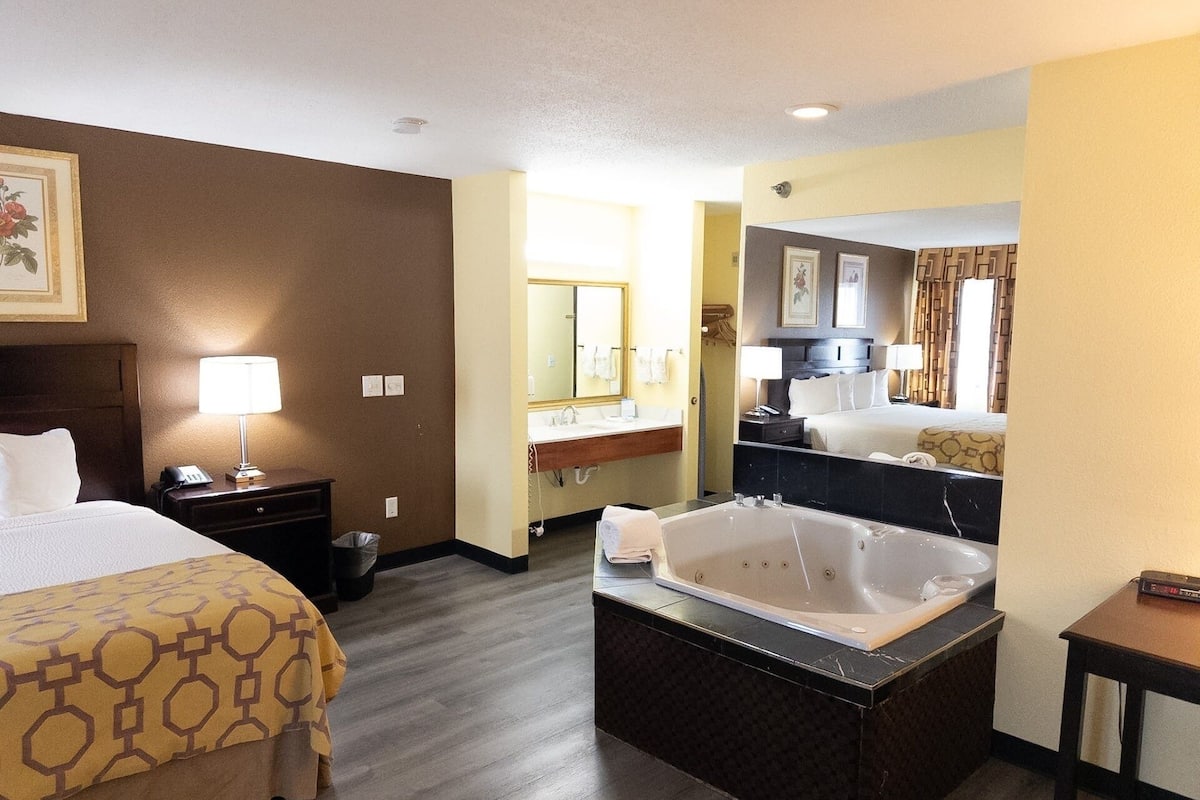 A hotel room with a bed, a bathroom with a bathtub, a vanity, and a mirror.