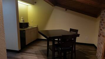 Une petite pièce peu éclairée, avec une table et des chaises en bois, un four à micro-ondes et un évier.
