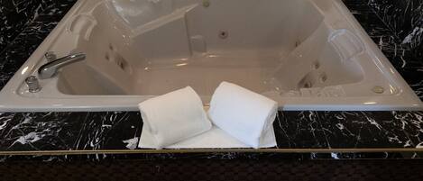 A rectangular bathtub with a single faucet, two towel holders with white towels, and a marble countertop.