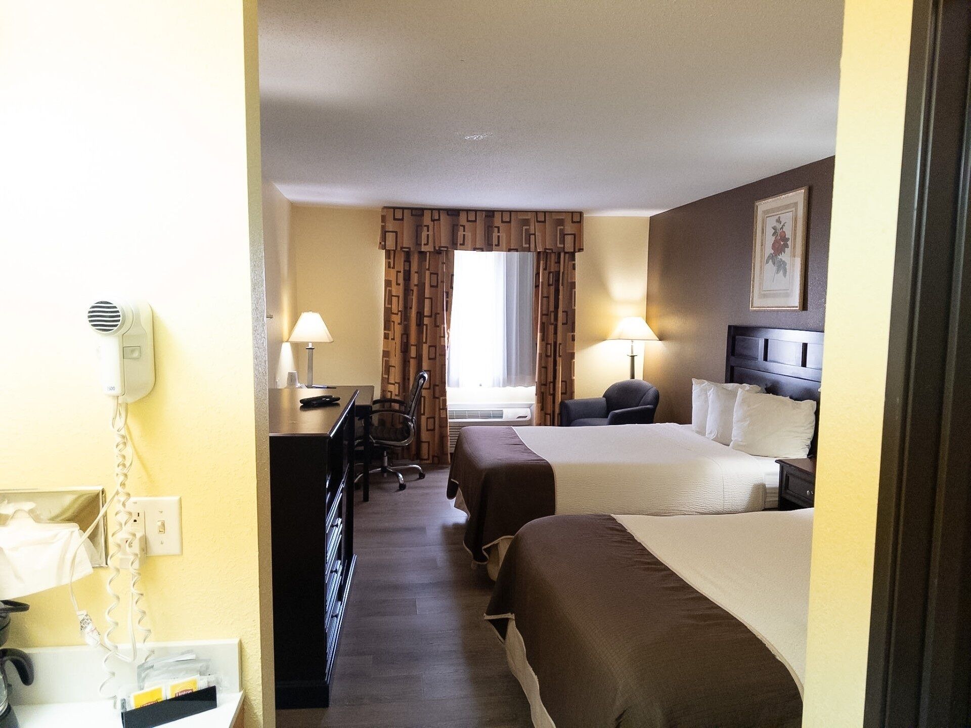 A hotel room with two beds, a desk, a chair, a lamp, and a telephone.