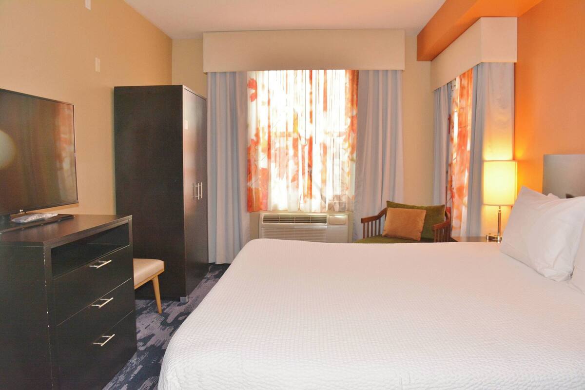 A hotel room with a large bed, a desk with a chair, a TV, and a wardrobe.