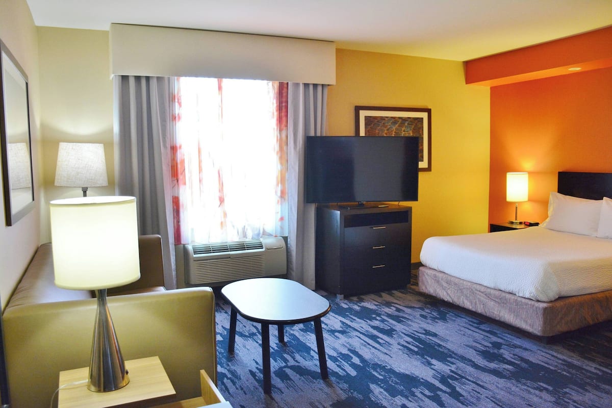 A hotel room with a bed, a desk, a chair, a television, and a window with curtains.