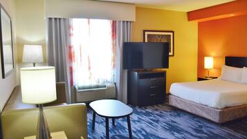 Una habitación de hotel con cama, escritorio, silla, televisor y ventana con cortinas.