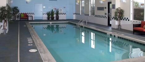 An indoor swimming pool with a checkered border, a lifeguard sign, and a red chair near the pool.