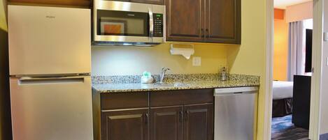 A kitchen with a stainless steel refrigerator, microwave, and dishwasher, wooden cabinets, granite countertop, and a visible towel rack.