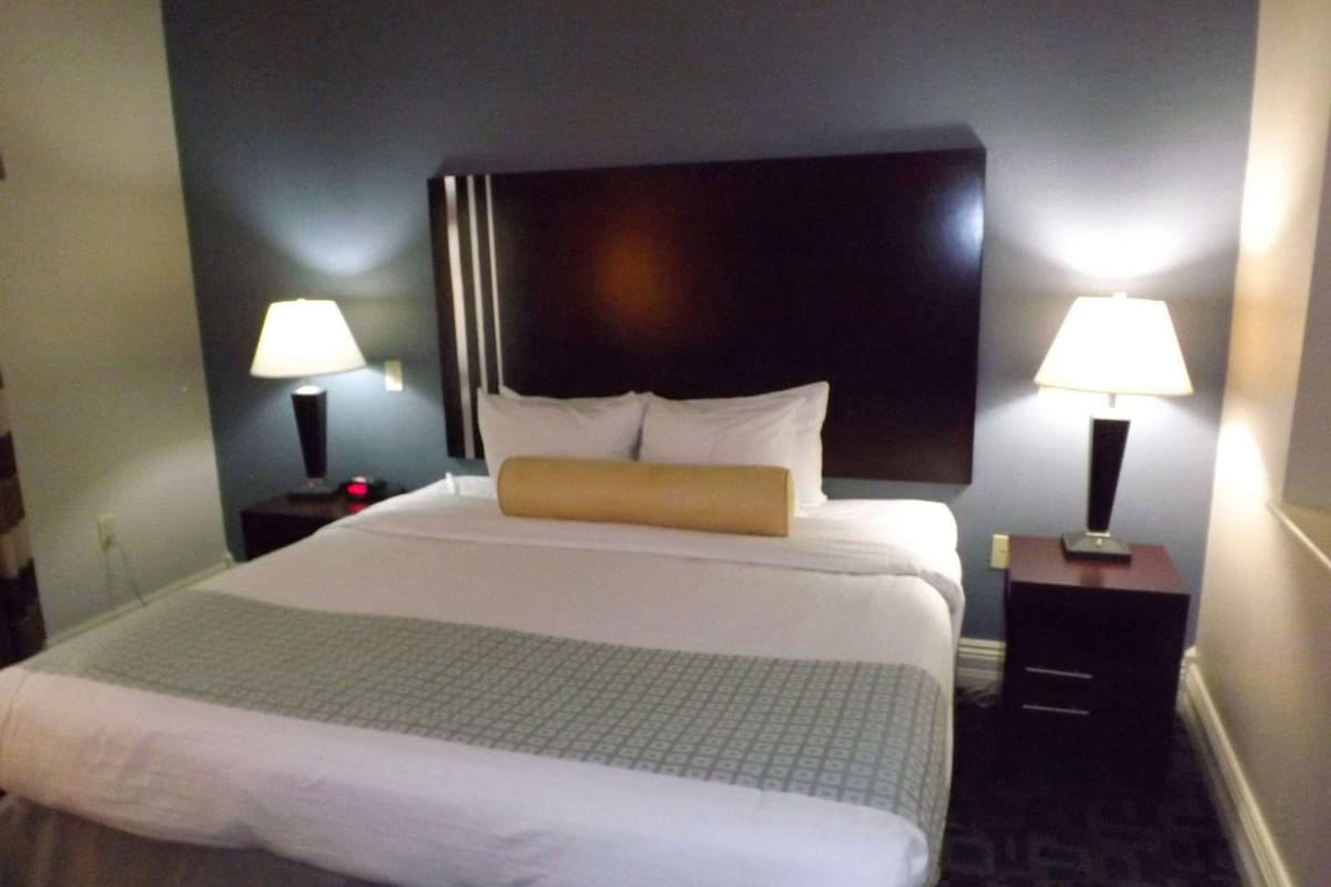 A hotel room with a large bed, two bedside tables with lamps, and a dark headboard.