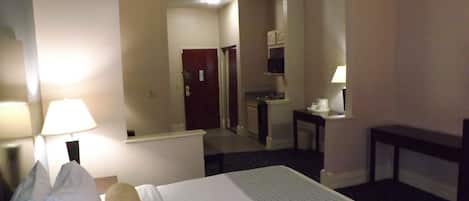 A hotel room with a bed, a desk, a chair, a lamp, and a mirror.