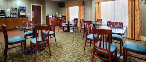 A hotel dining area with wooden chairs and tables, a coffee machine, and a refrigerator.