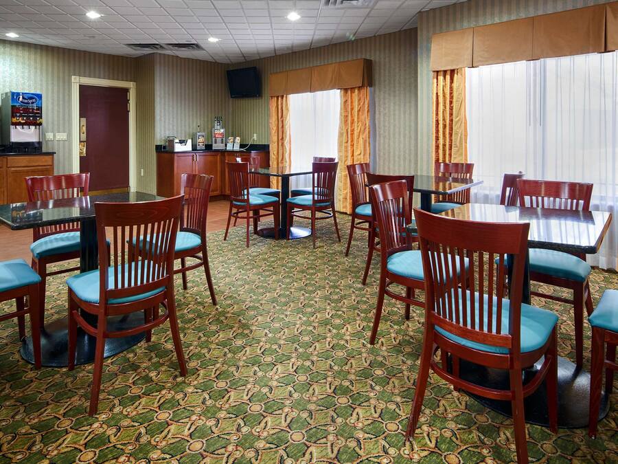 Un comedor de hotel con sillas y mesas de madera, una máquina de café y un refrigerador.