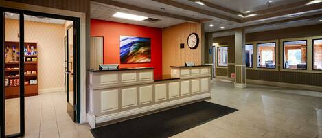 Un hall d’hôtel avec un comptoir d’accueil, une horloge et un mur orné d’un tableau abstrait aux couleurs vives.