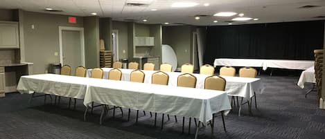 Uma sala de conferência com várias mesas e cadeiras, uma copa e uma área de palco.
